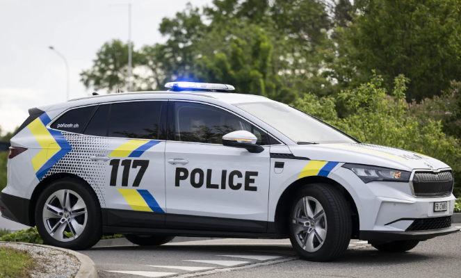 Voiture de police suisse blanche avec le numéro 117, garée sur le bord de la route avec des arbres en arrière-plan.