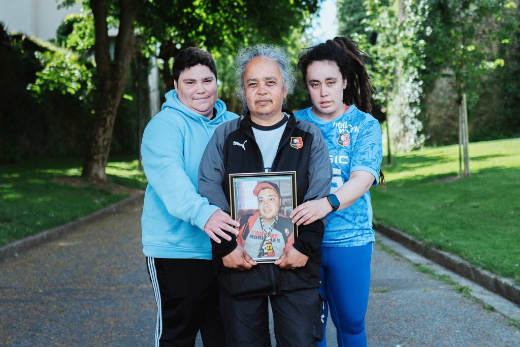 Trois femmes racisées tiennent la photo encadrée d'un jeune homme racisé.
